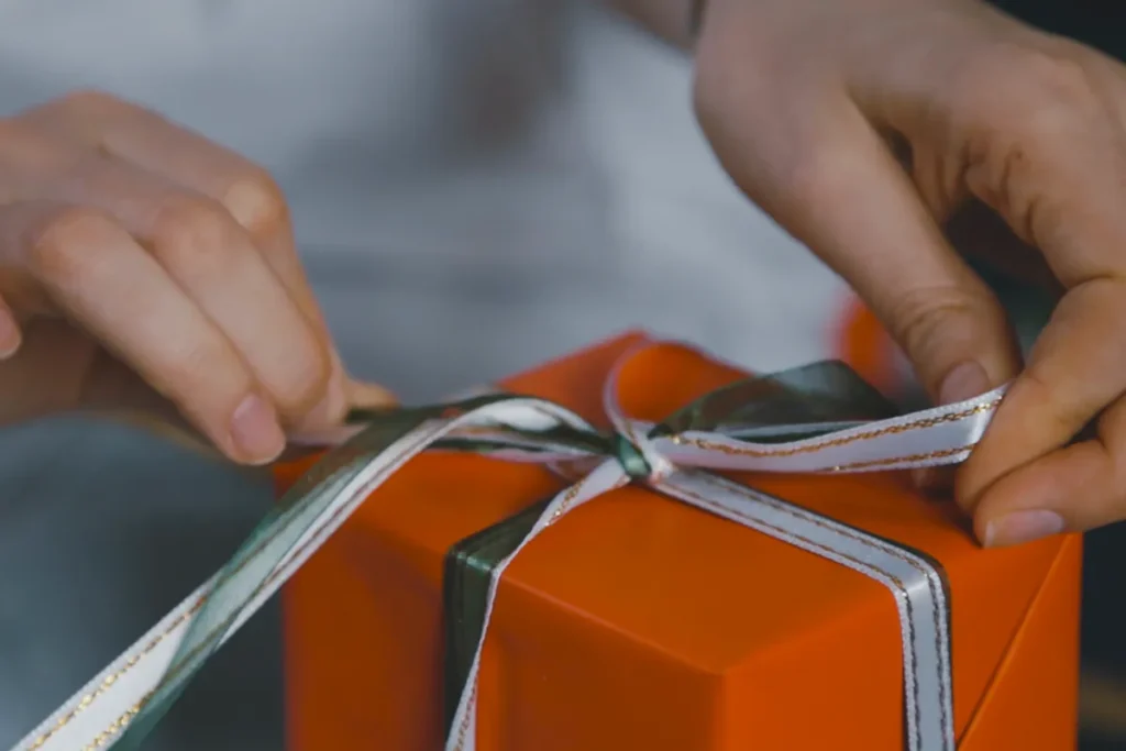 Hands finishing a satin bow on a gift box